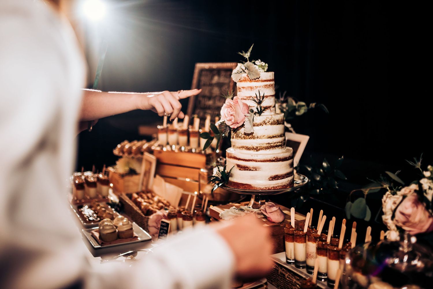 Wedding dessert table with tiered naked cake and candles in dark lighting.