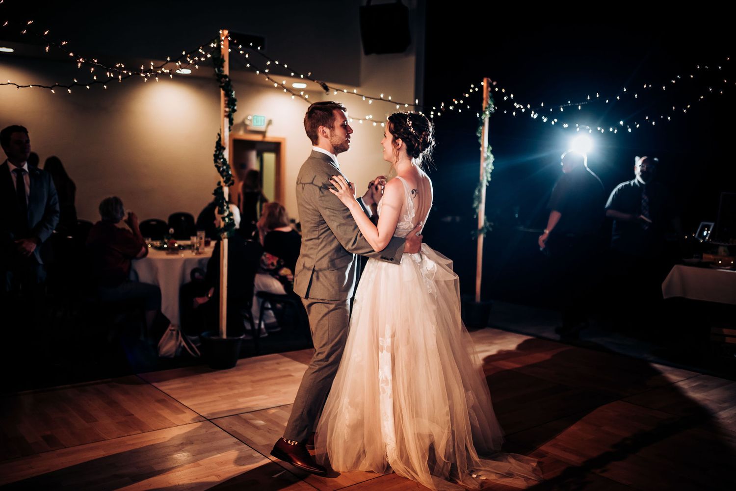 Couple dances together beneath string lights during wedding reception.