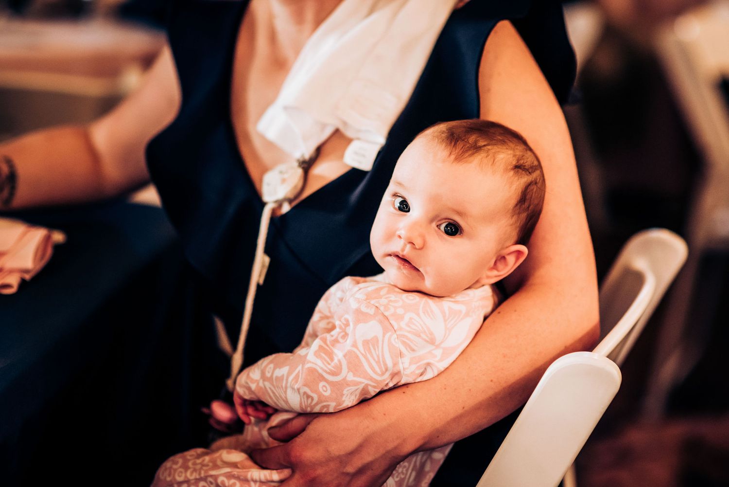 Small baby in lace outfit sitting at formal dinner table during celebration.