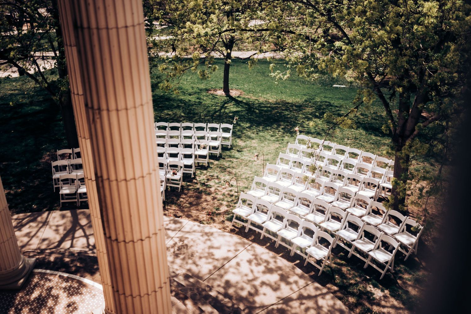 White wedding ceremony chairs arranged outdoors under pillared structure.