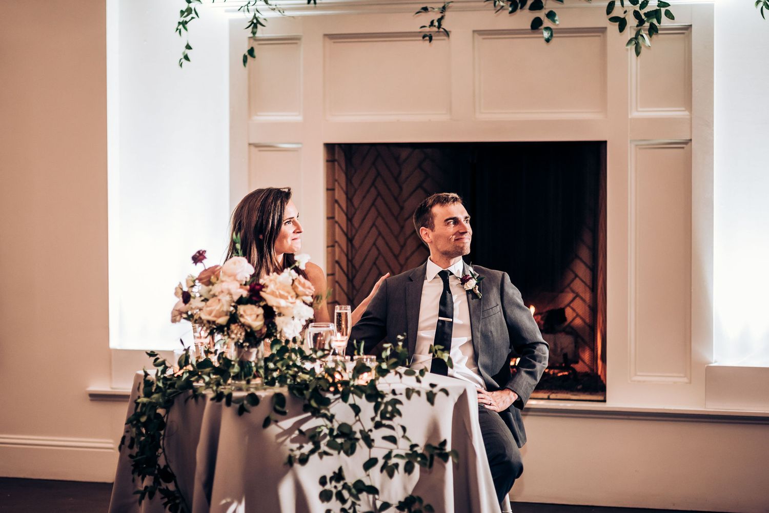 Couple shares a moment at their sweetheart table decorated with cascading greenery.