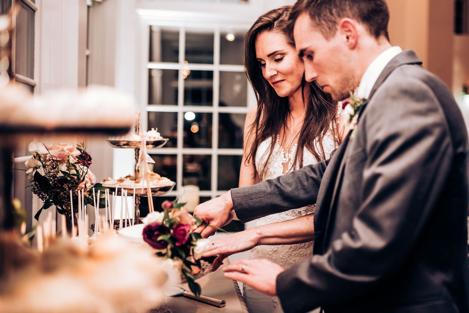A couple leans in close while cutting their wedding cake together at an elegant reception.