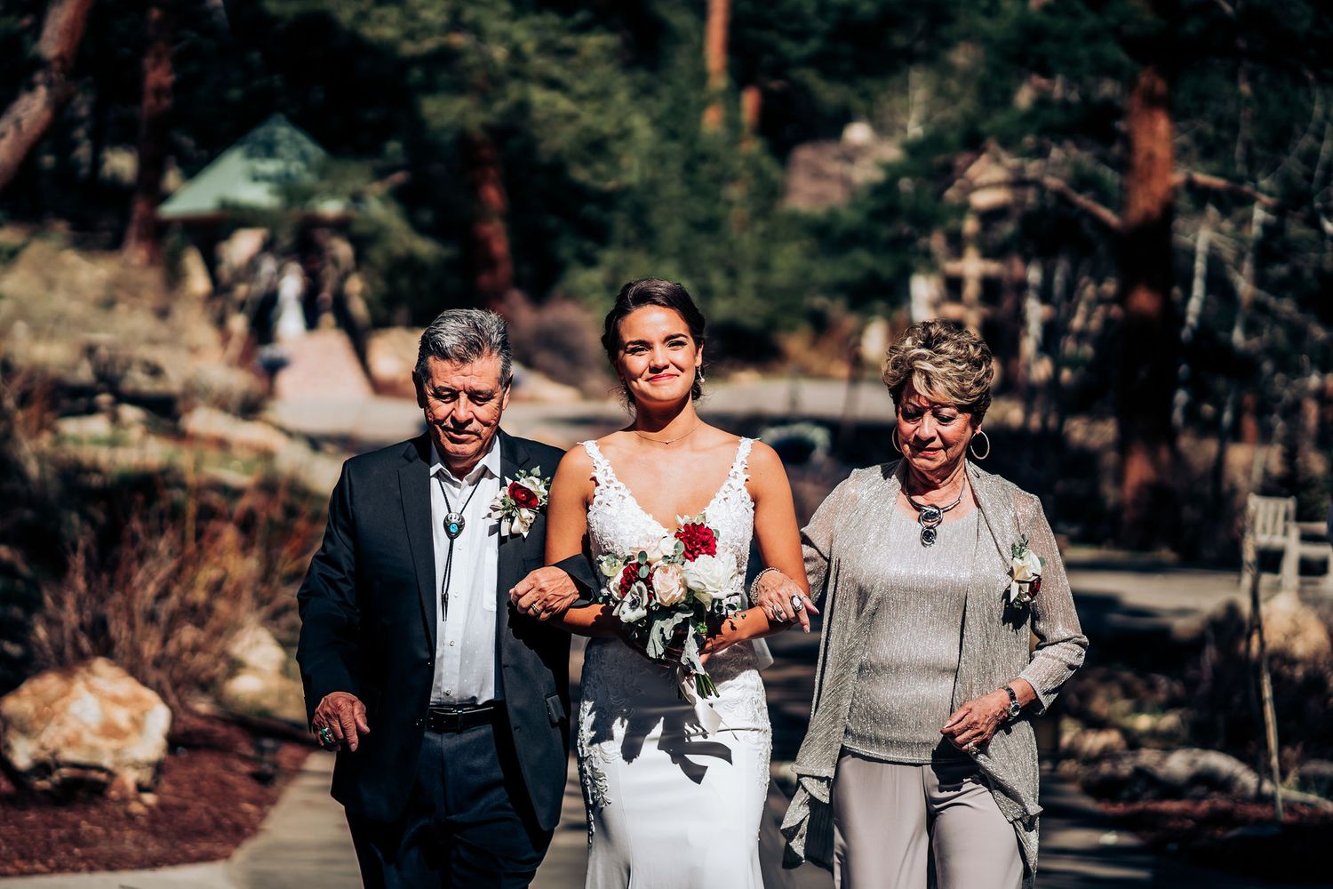 Wedding processional walking down sunny outdoor pathway in mountain setting.