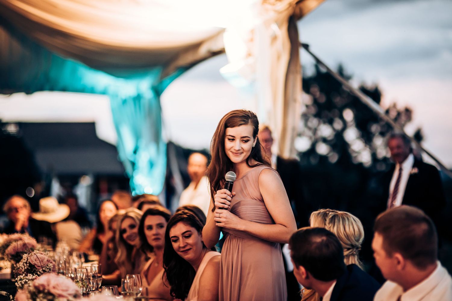 A bridesmaid in a pink dress gives an emotional speech at an outdoor wedding reception.