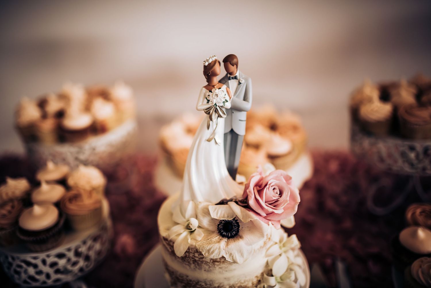 Wedding cake topper figurine surrounded by pink roses and chocolate cupcakes.