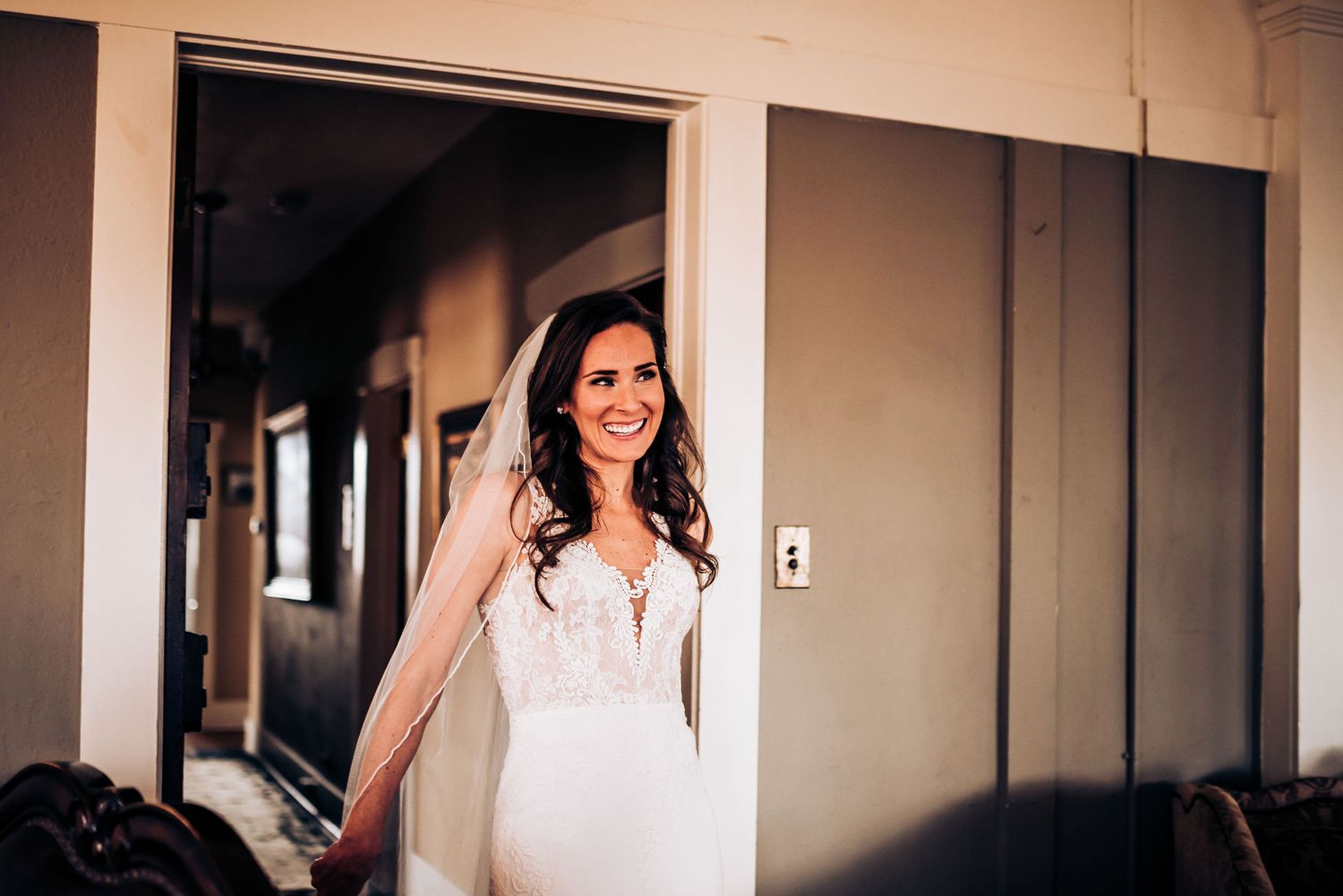 A lace wedding gown with delicate details illuminated in a hallway setting against neutral walls.