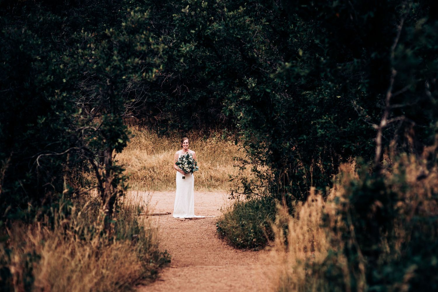 A figure in a flowing white dress walks along a dirt trail surrounded by autumn foliage.