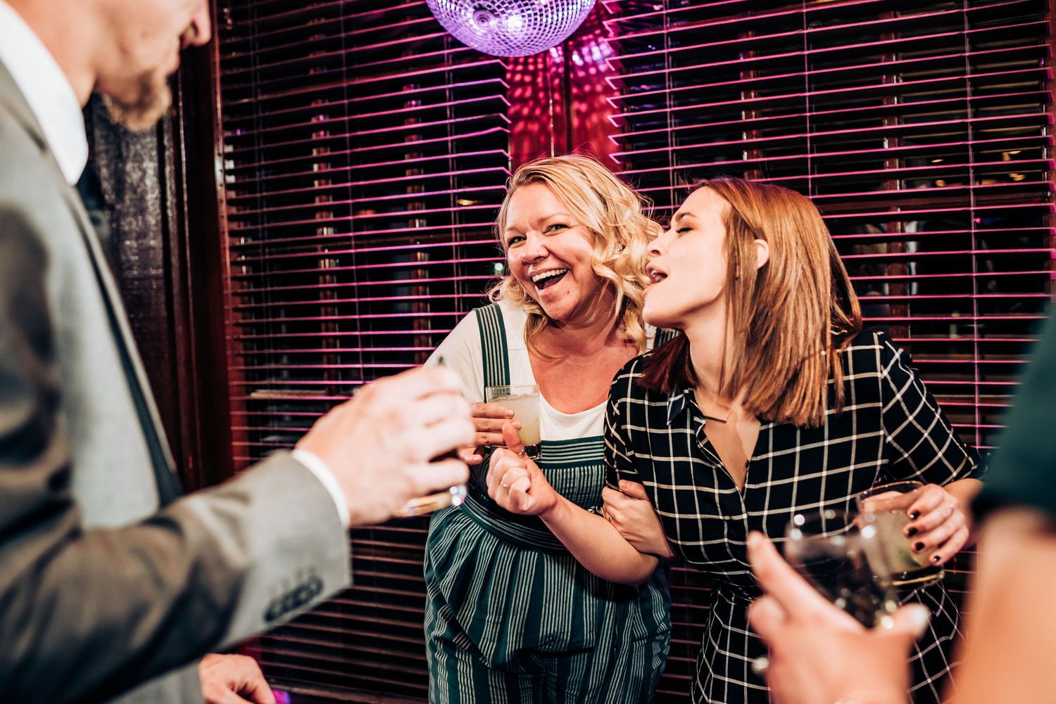 Party guests laughing and celebrating under a pink disco ball at a dimly lit indoor venue.