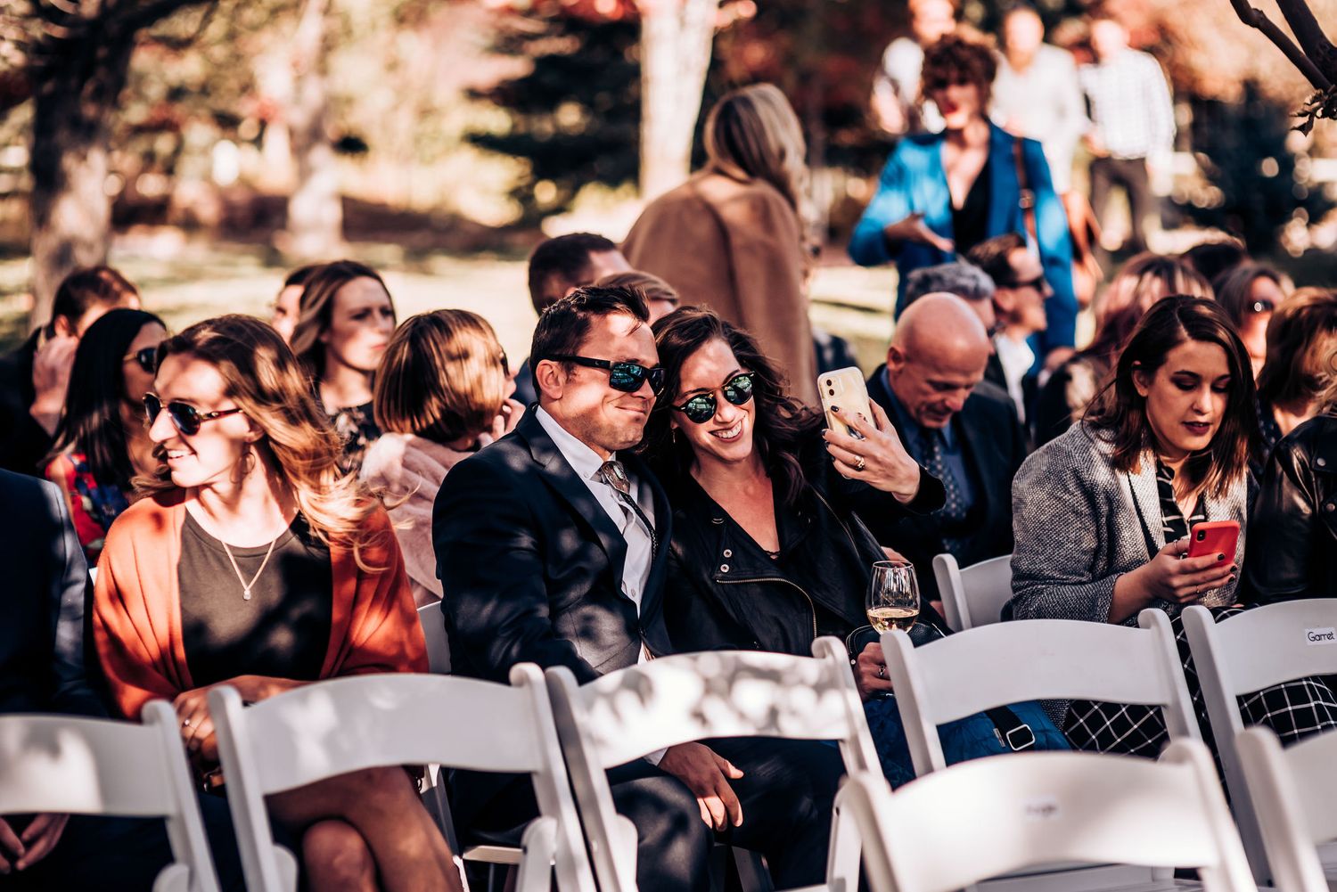 Wedding guests seated in white chairs during an outdoor autumn ceremony.