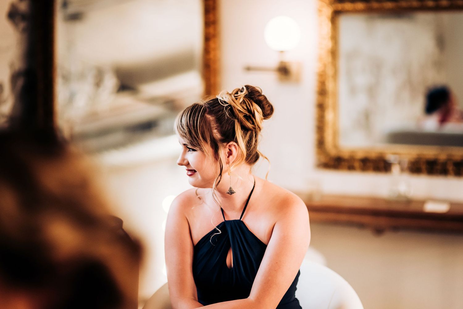 Someone in an elegant black dress smiles while sitting in a vintage-style room.