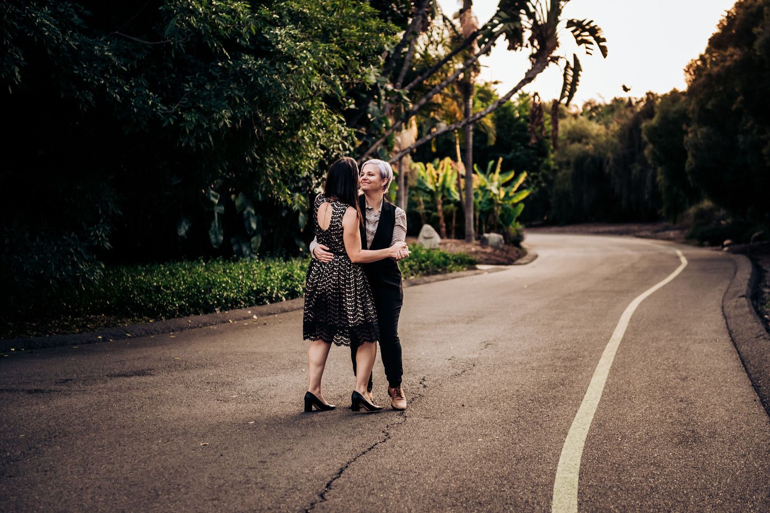 Two people embrace while dancing on a curved garden path at sunset.