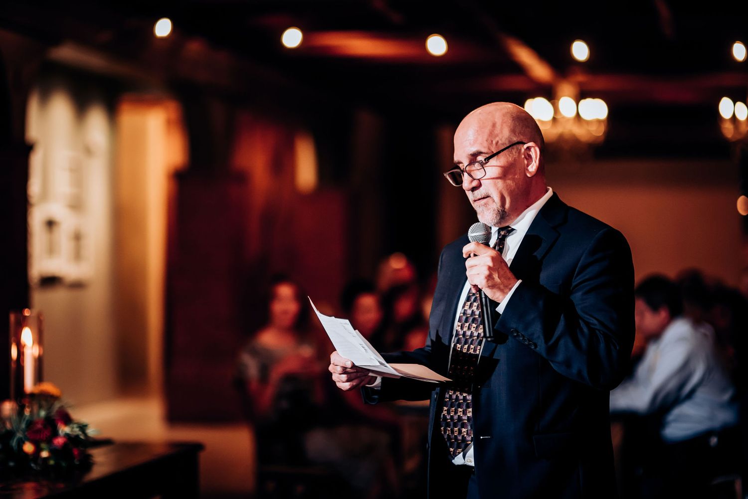 Public speaker giving a speech at an indoor event with warm ambient lighting.