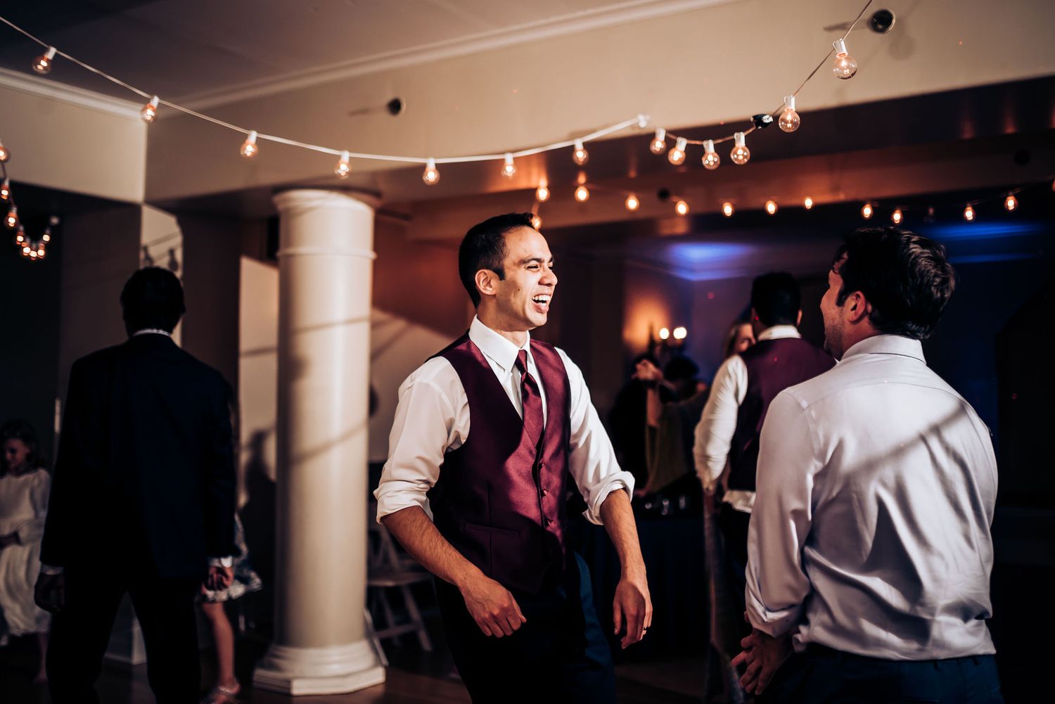 View of a dimly lit reception venue with string lights and white columns.