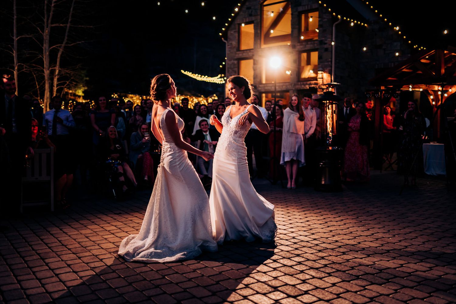 Two people in elegant white gowns dancing together at an outdoor reception.