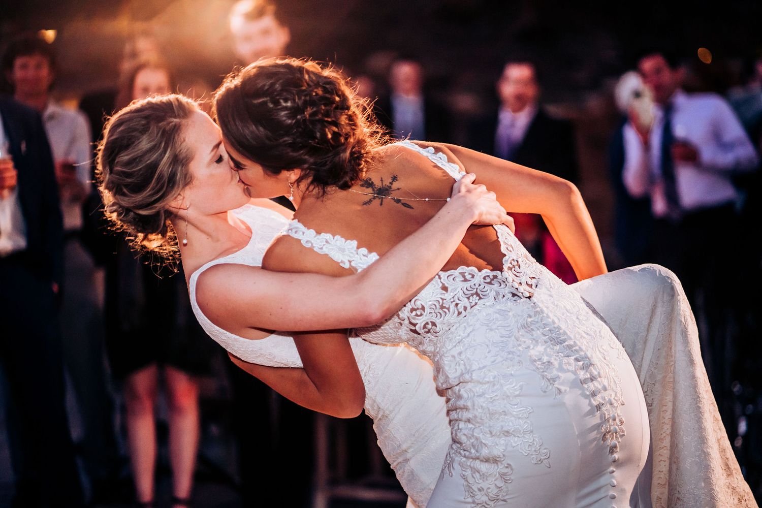 A romantic first dance at a wedding reception shows two brides in white dresses dipping on the dance floor.