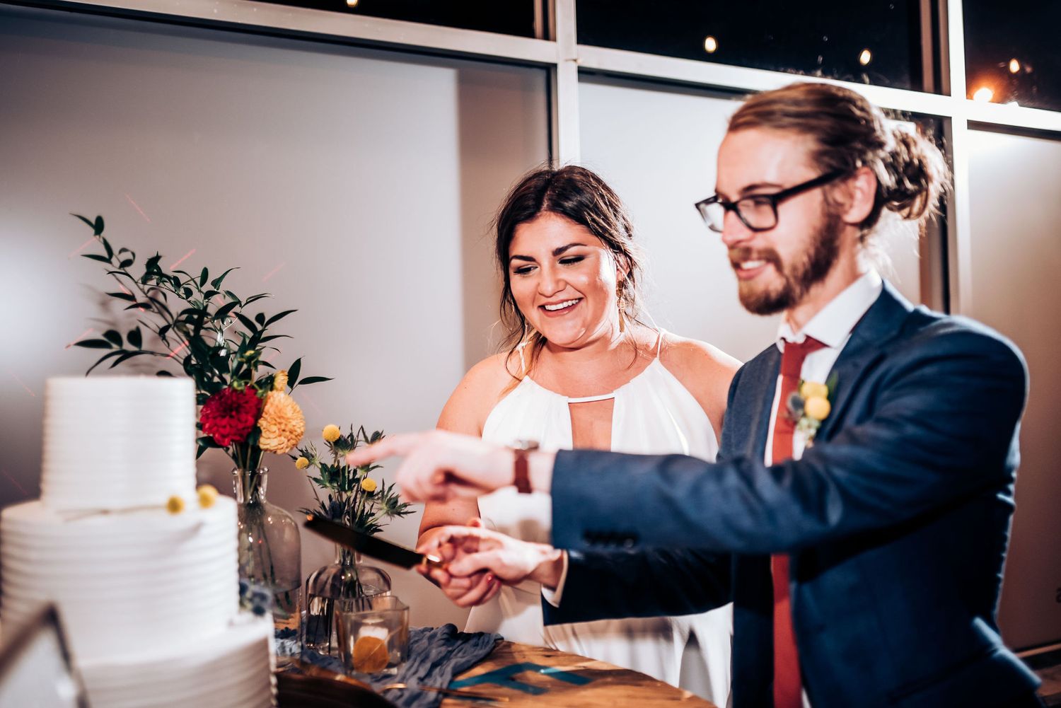 Wedding couple cuts their elegant white tiered cake together at reception.