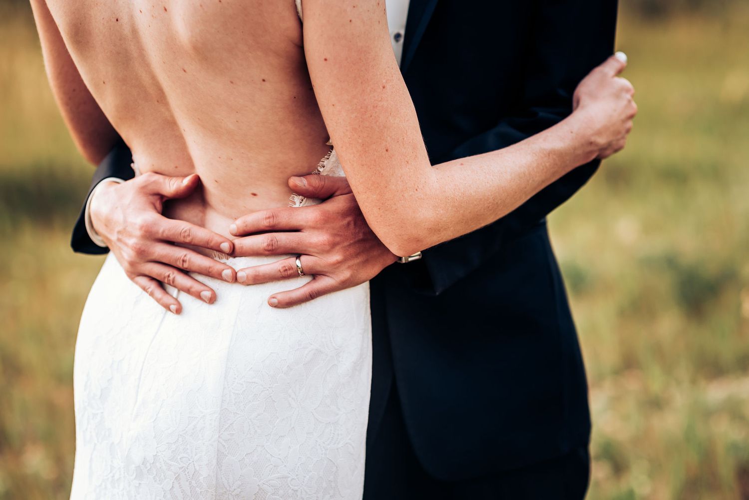 Close-up of newlyweds embracing, showing details of wedding dress and suit.