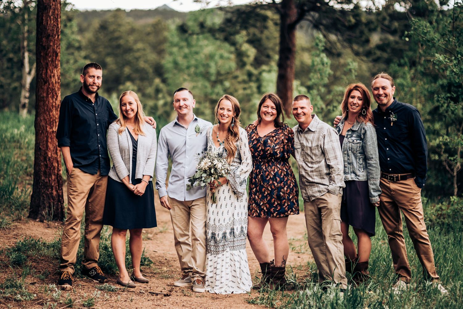 A group stands together outdoors for a formal photo among pine trees.