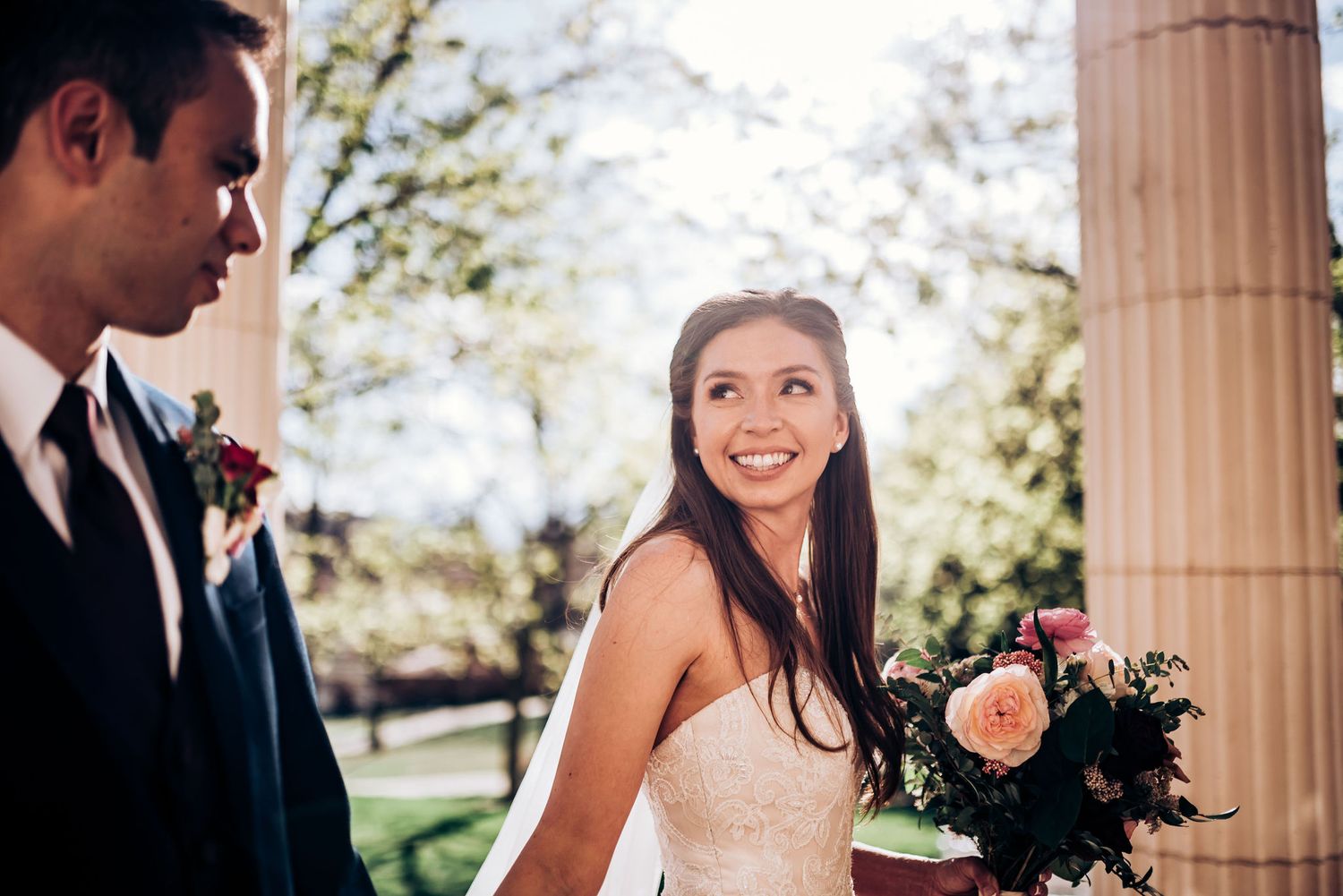 Joyful wedding moment captured between architectural columns in natural light.