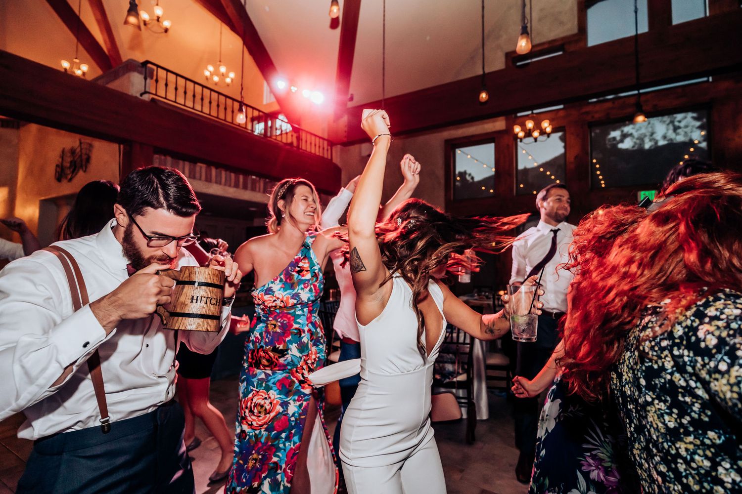 Energetic dance party at a wedding reception with guests in formal attire under red lighting.