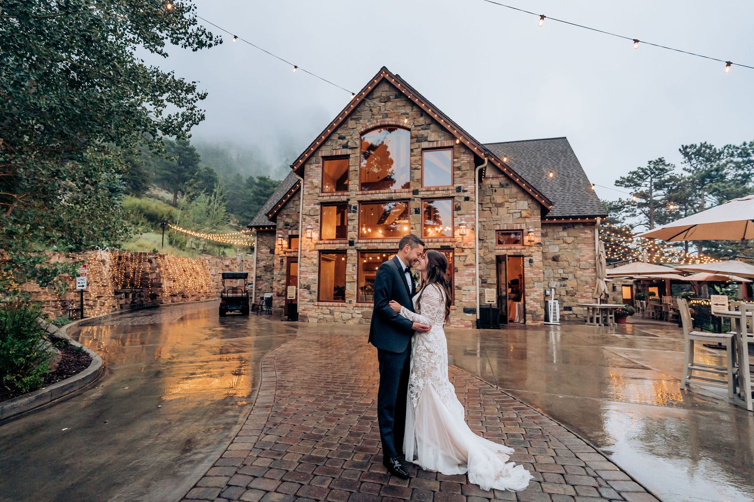 Newlyweds pose in front of rustic stone venue on rainy wedding day.