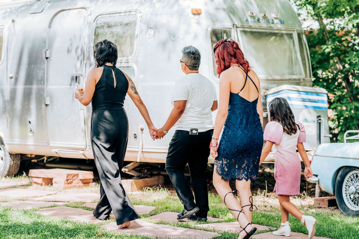 Group walking together towards a silver Airstream trailer on a sunny day.