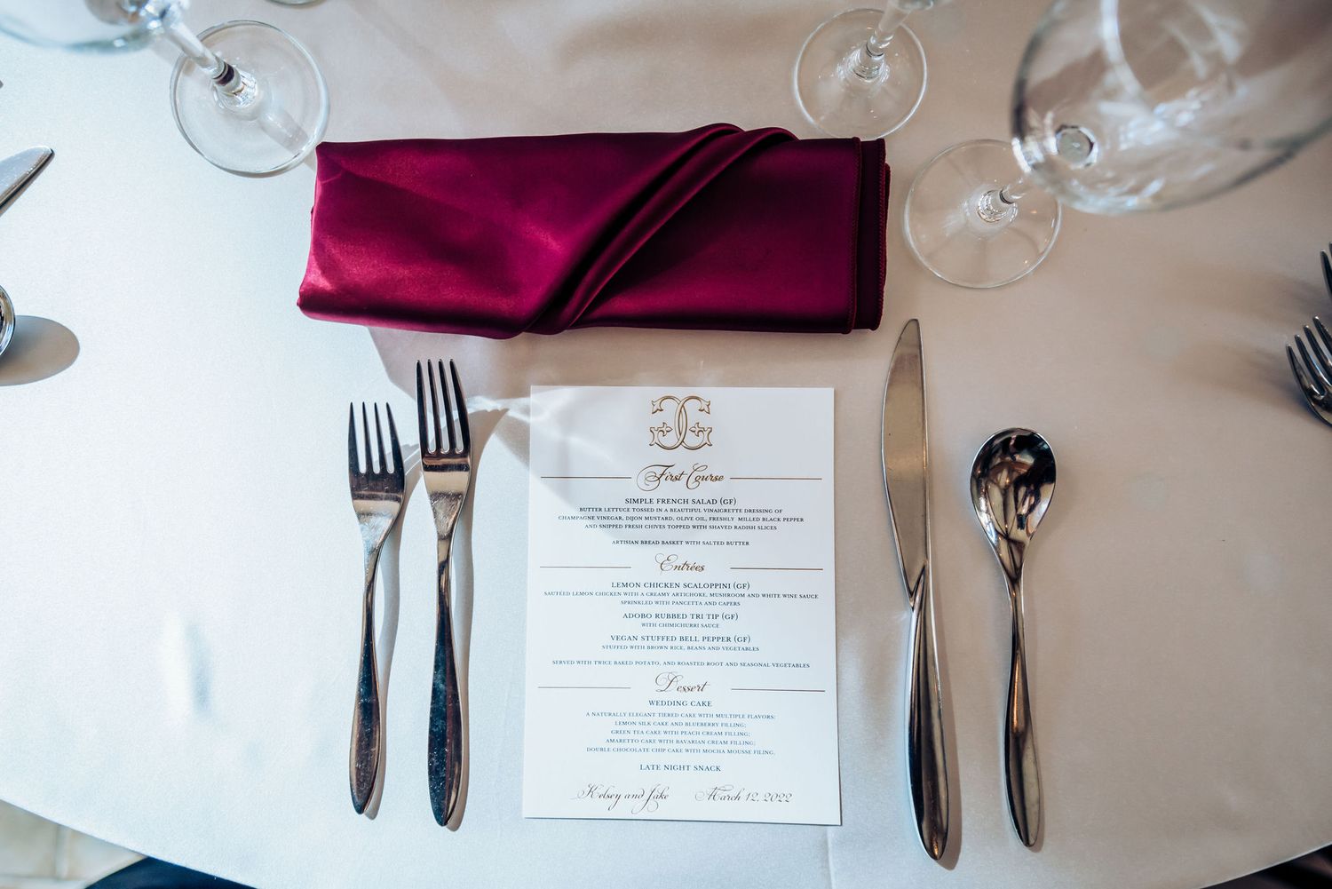 Elegant place setting with burgundy napkin and menu card on white tablecloth with silverware.