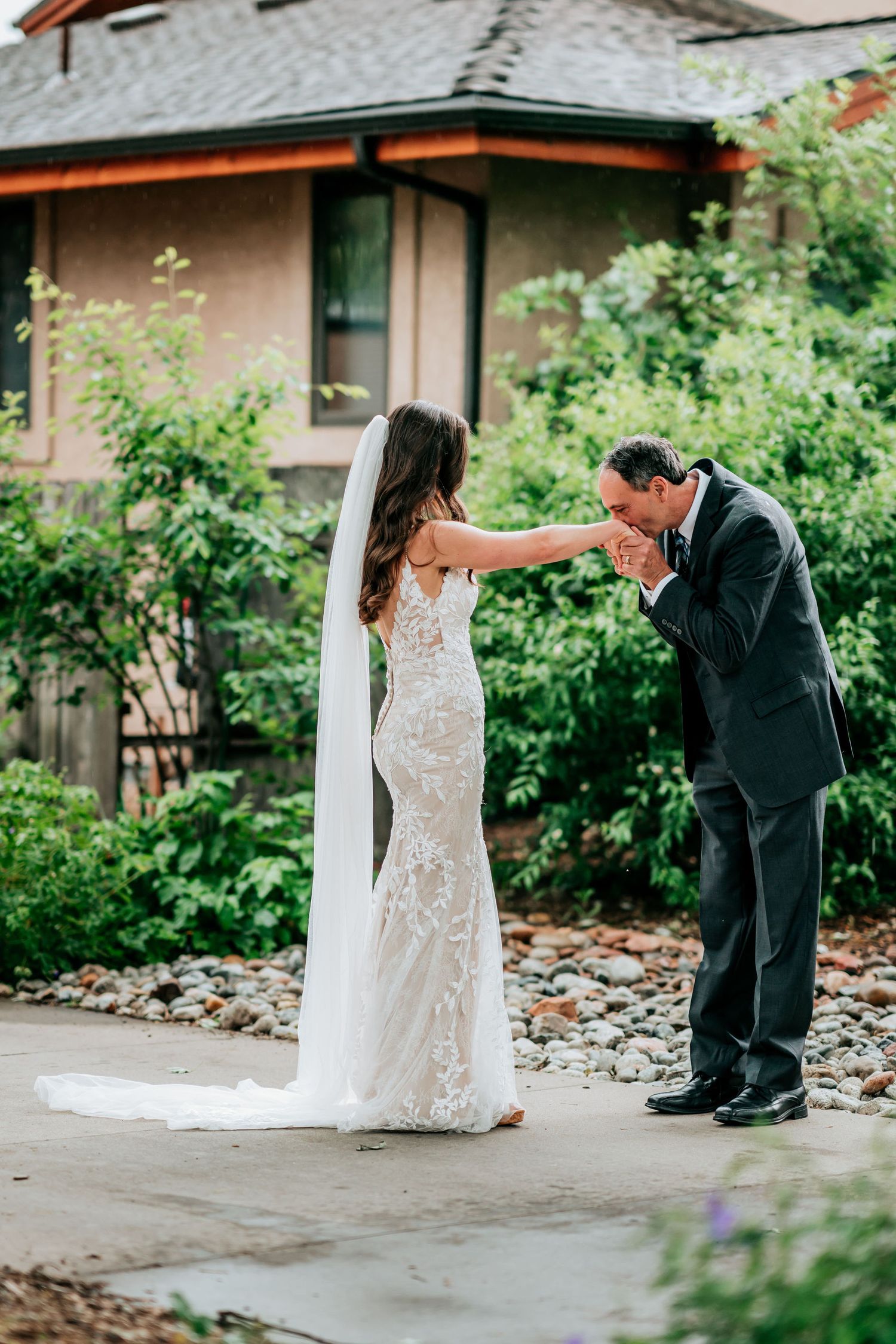 A touching wedding moment captured as the groom kisses the bride's hand on a garden pathway.