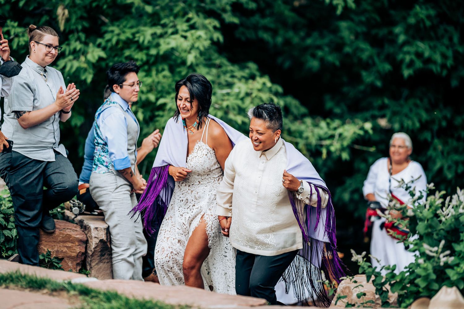Joyful celebration on stone steps during an outdoor wedding with greenery in the background.