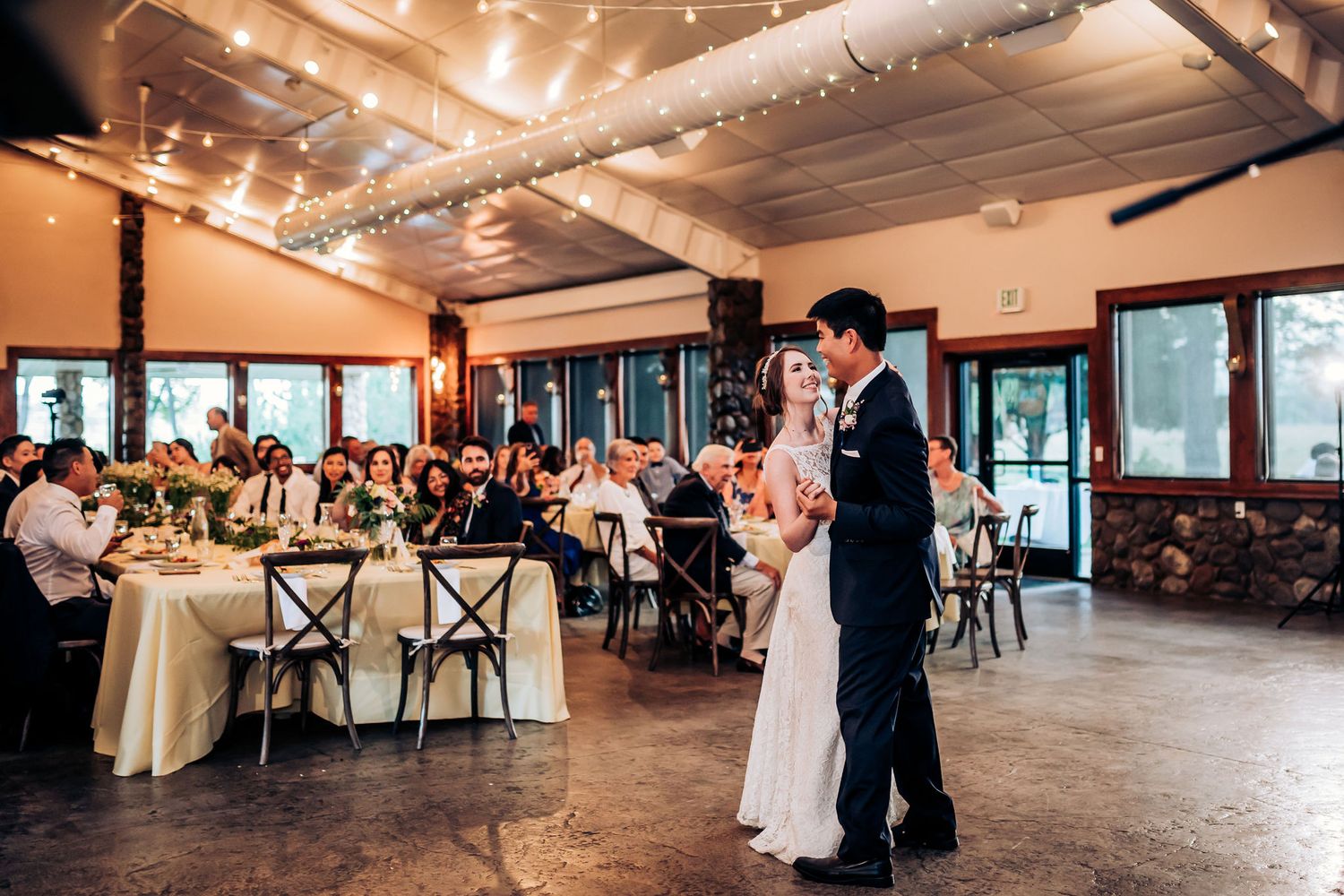 A couple shares an intimate dance moment at their wedding reception under twinkling lights.