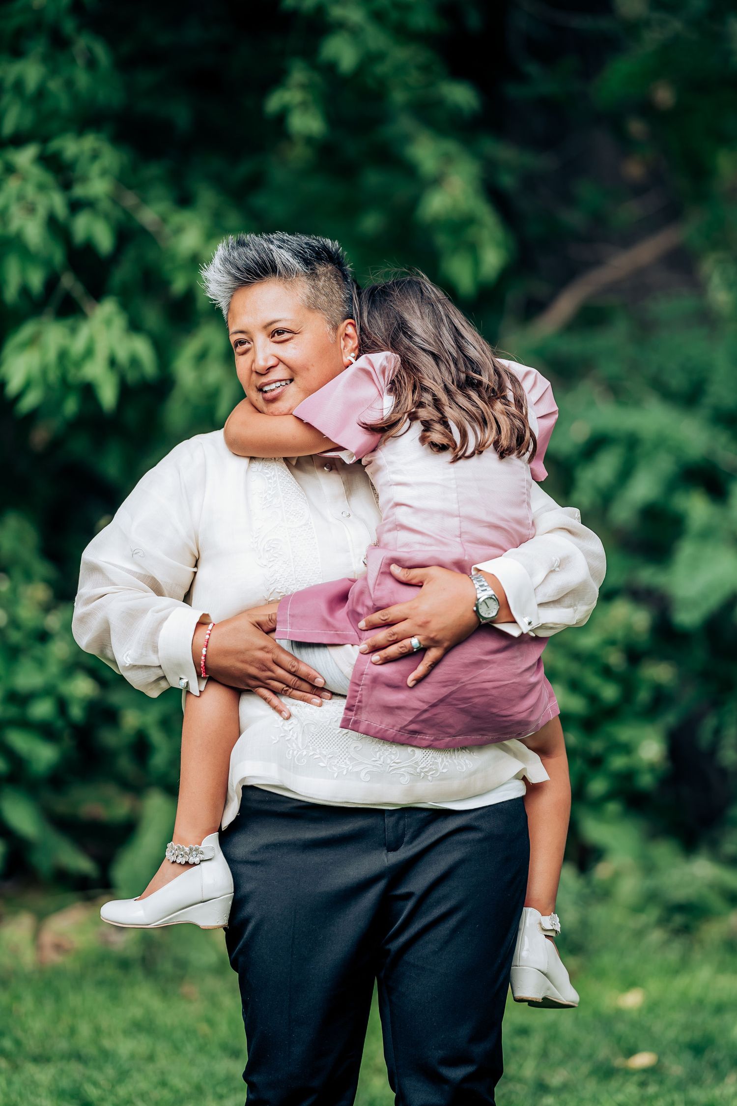 Tender moment captured between two people in an outdoor setting with lush green foliage.