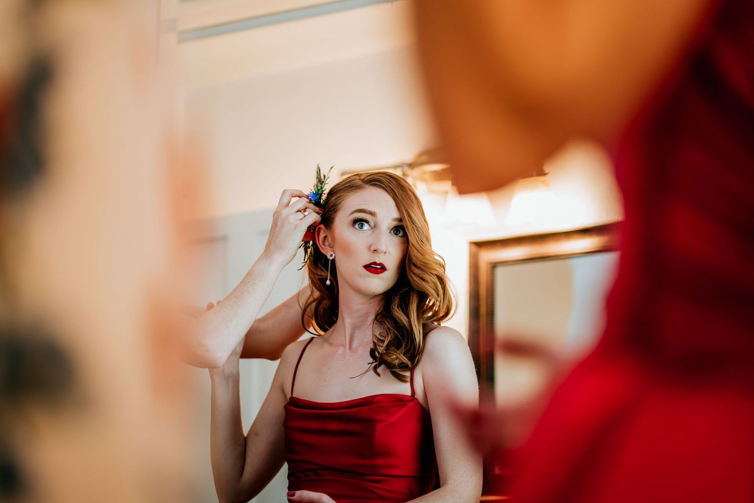 Someone in a red dress applies makeup while looking in a mirror with surprised expression.