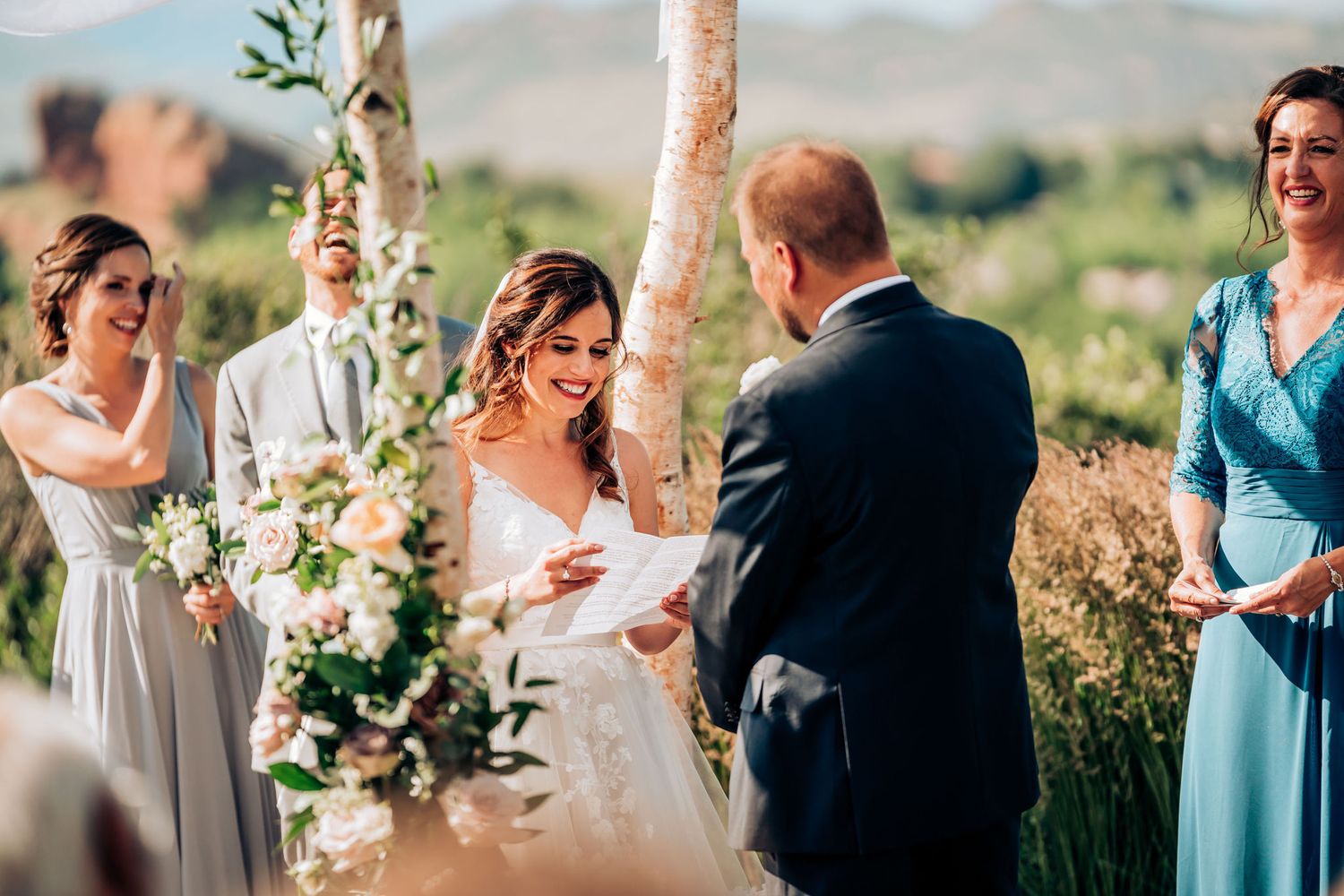 Outdoor wedding ceremony with white birch arch and floral decorations against mountain backdrop.