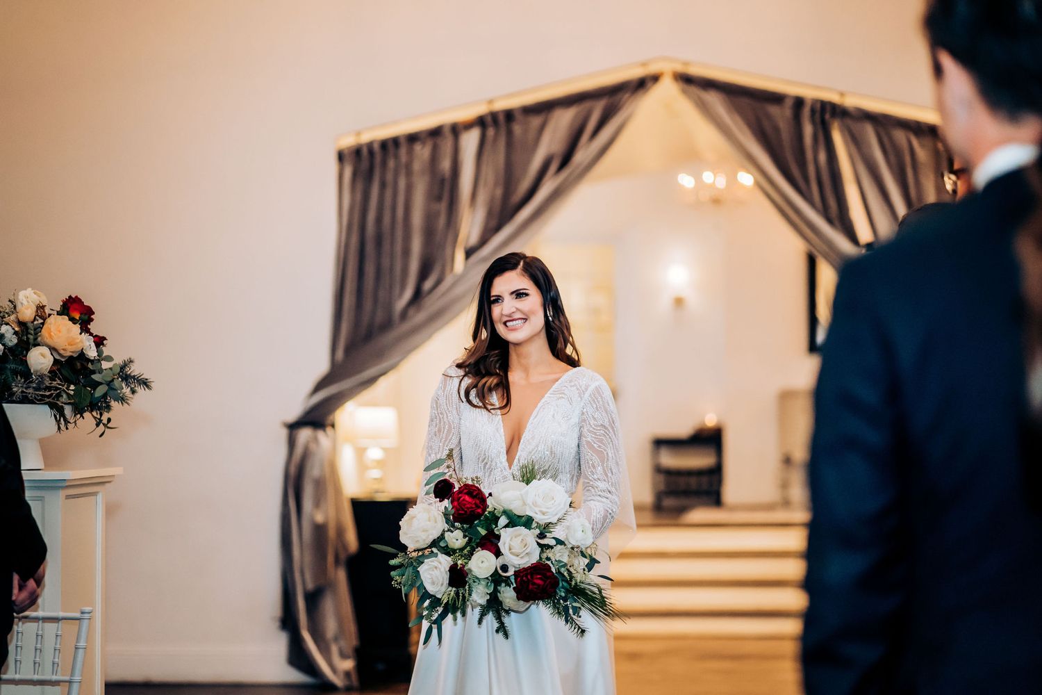 A bride in a white dress holds a bouquet while standing in an elegant venue entrance.
