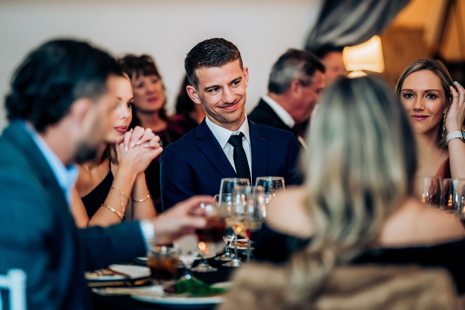 Elegant wedding reception dinner with guests engaging in conversation around formal table settings.