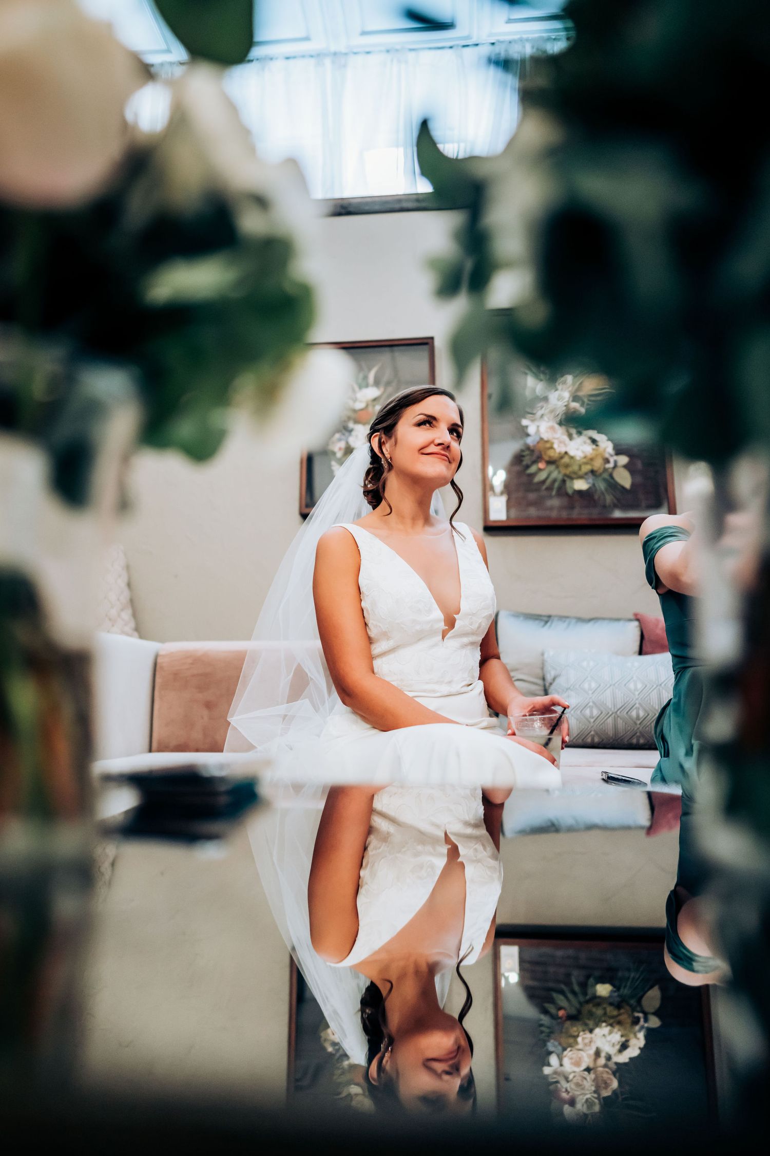 Artistic framed shot of a bride in white dress through greenery and decor.
