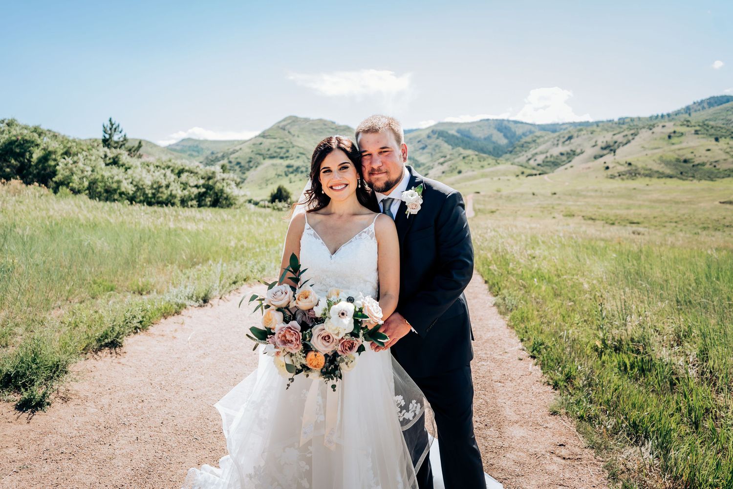 A newlywed couple poses together on a scenic mountain trail.