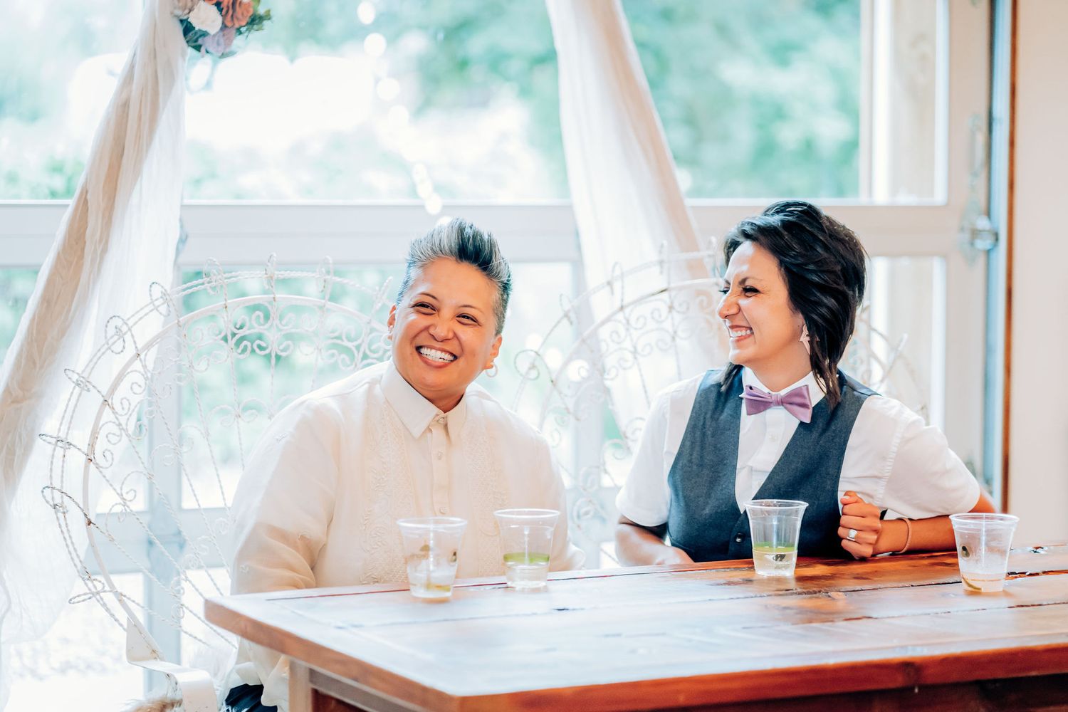 Two people in formal attire share a joyful moment while seated at a reception table.