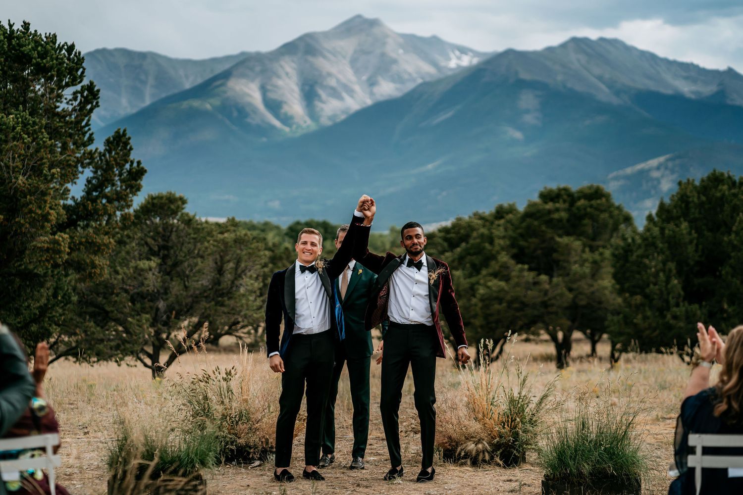 A celebratory moment at an outdoor wedding with mountains and trees in the background.