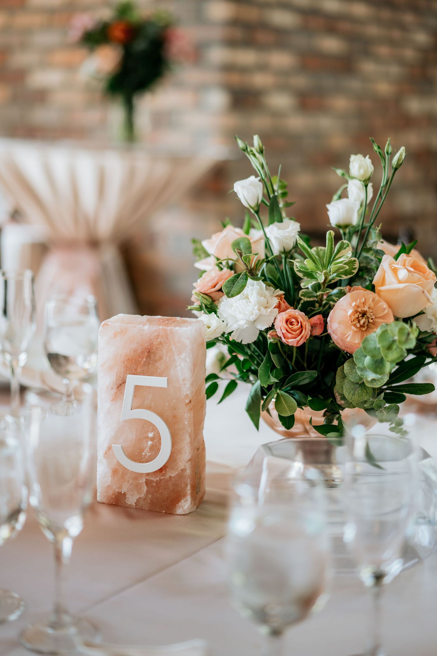 Wedding table decor featuring peach and white floral arrangement with table number five.