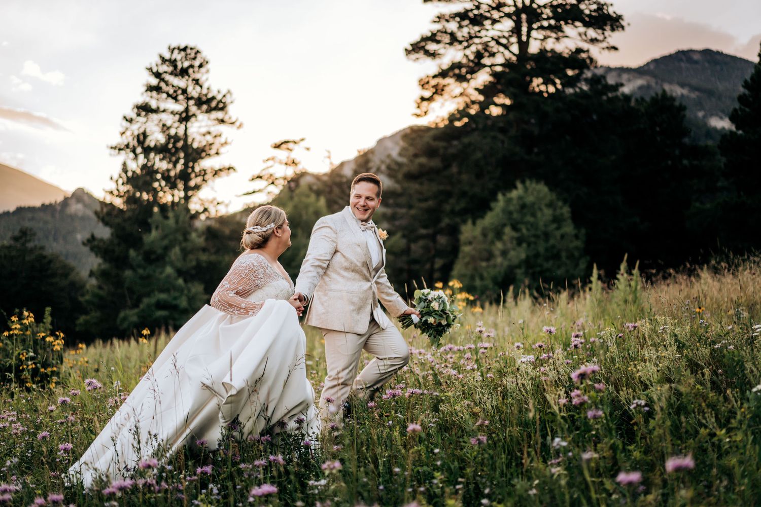 Wedding couple walks through mountain wildflower meadow at sunset.