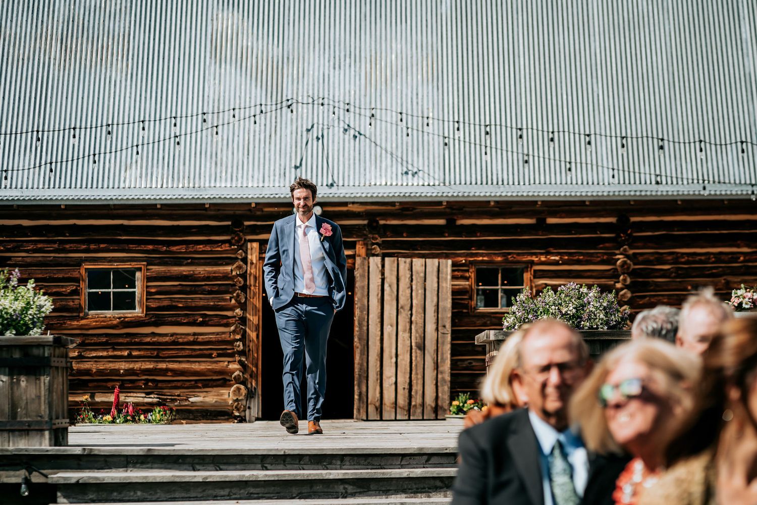 Guest stands on wooden steps of a rustic venue during an outdoor wedding celebration.