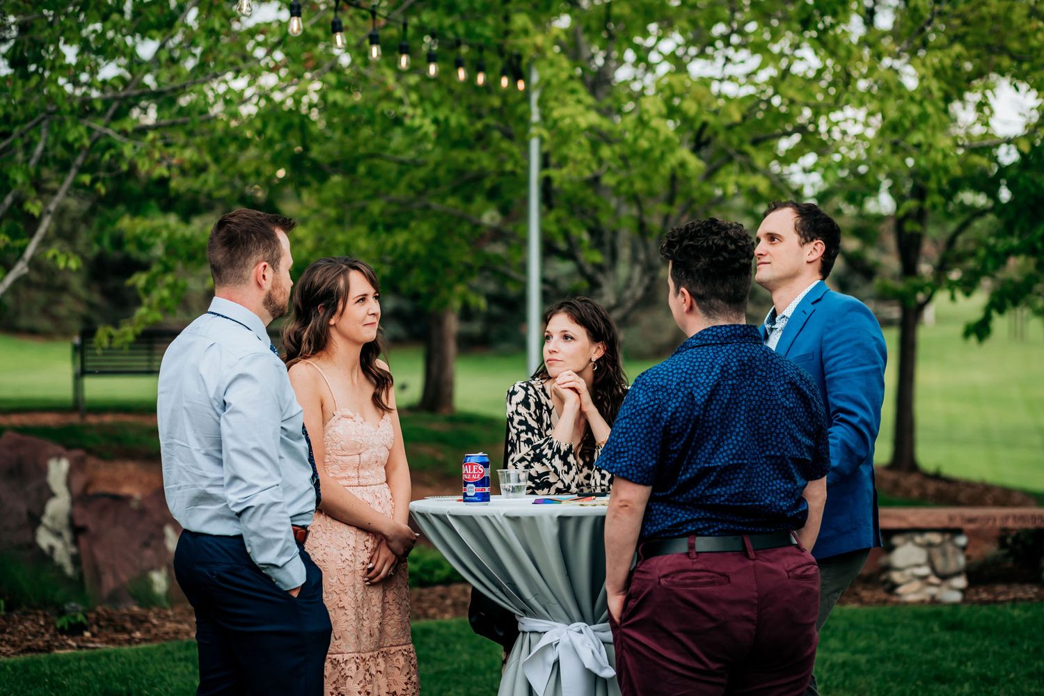 Small group of wedding guests chatting at cocktail hour by high table.