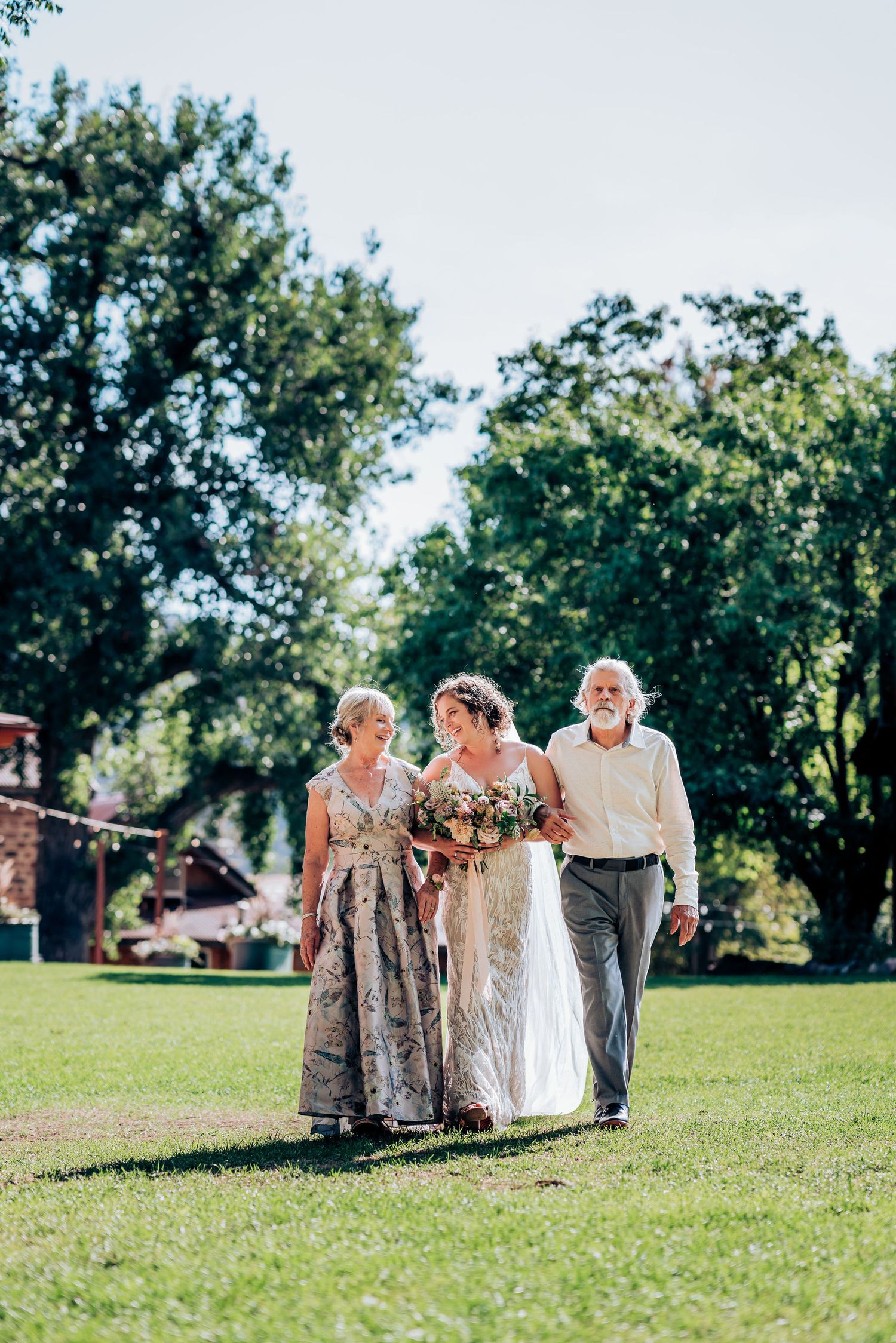 Wedding processional on green lawn with elegant attire and floral bouquet.