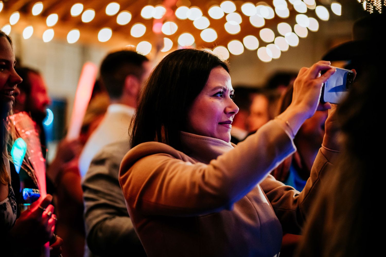 Guest takes photos with smartphone at an event with bokeh lights in background.