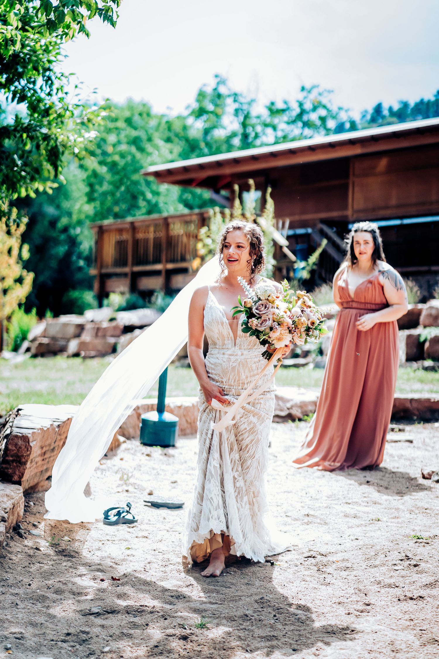 A beautiful outdoor wedding scene with flowing white dress and bouquet against rustic backdrop.