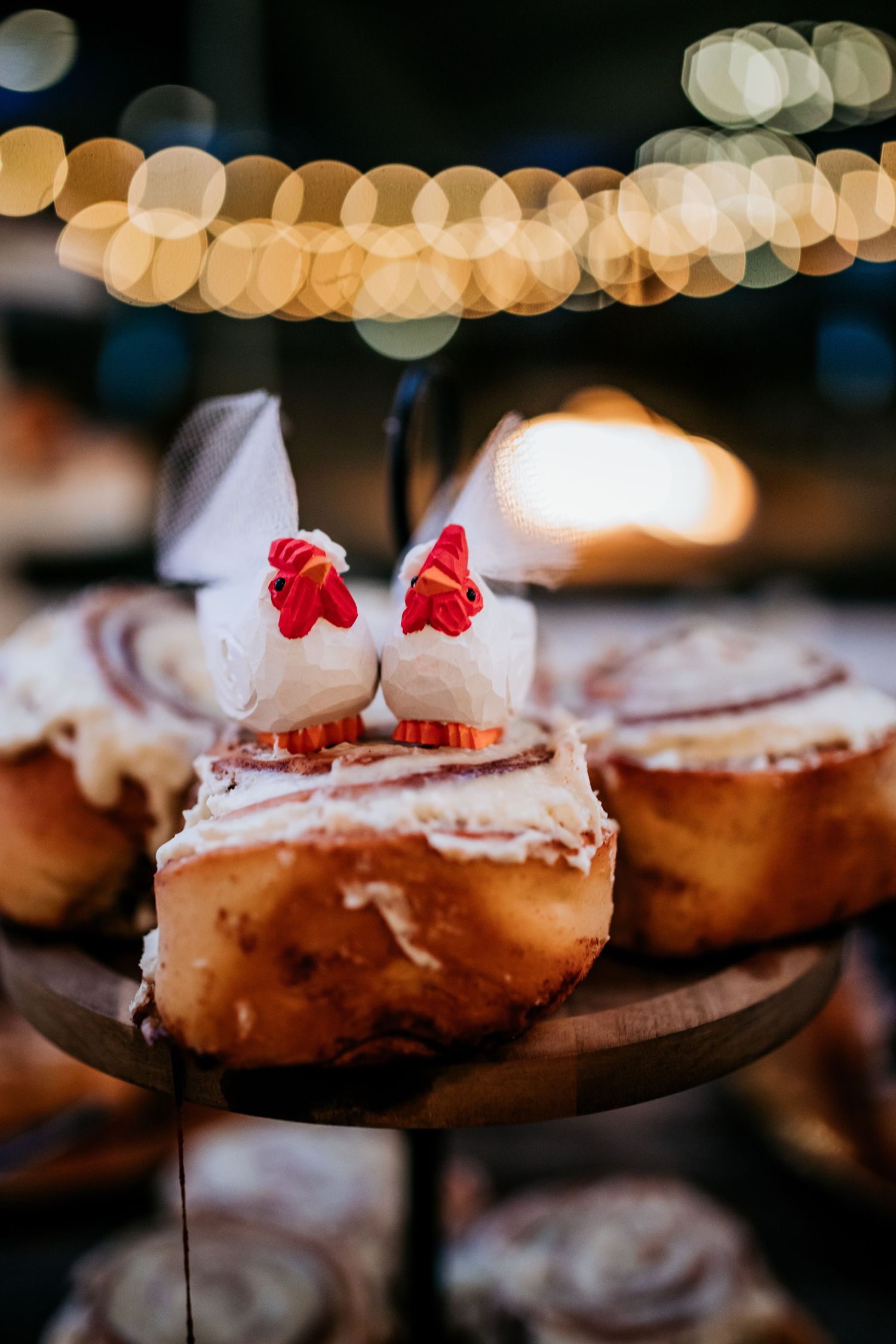 Wedding cinnamon rolls displayed on a wooden stand topped with two white chicken cake toppers.