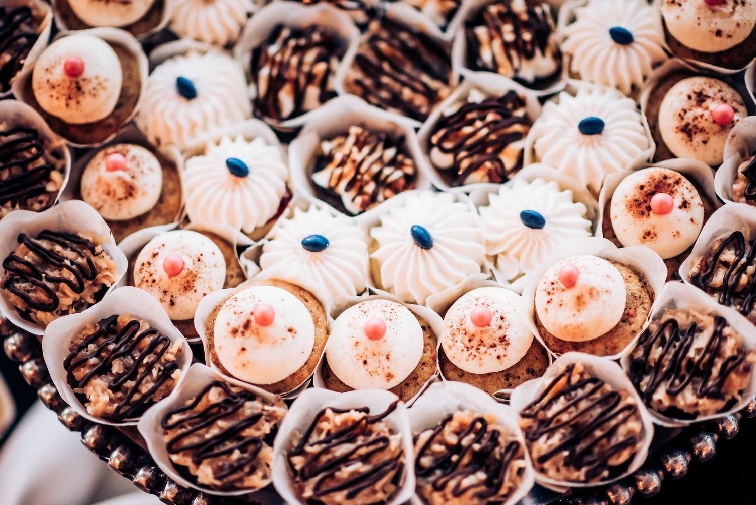 Overhead view of decorated chocolate and vanilla mini cupcakes with sprinkles arranged on display.