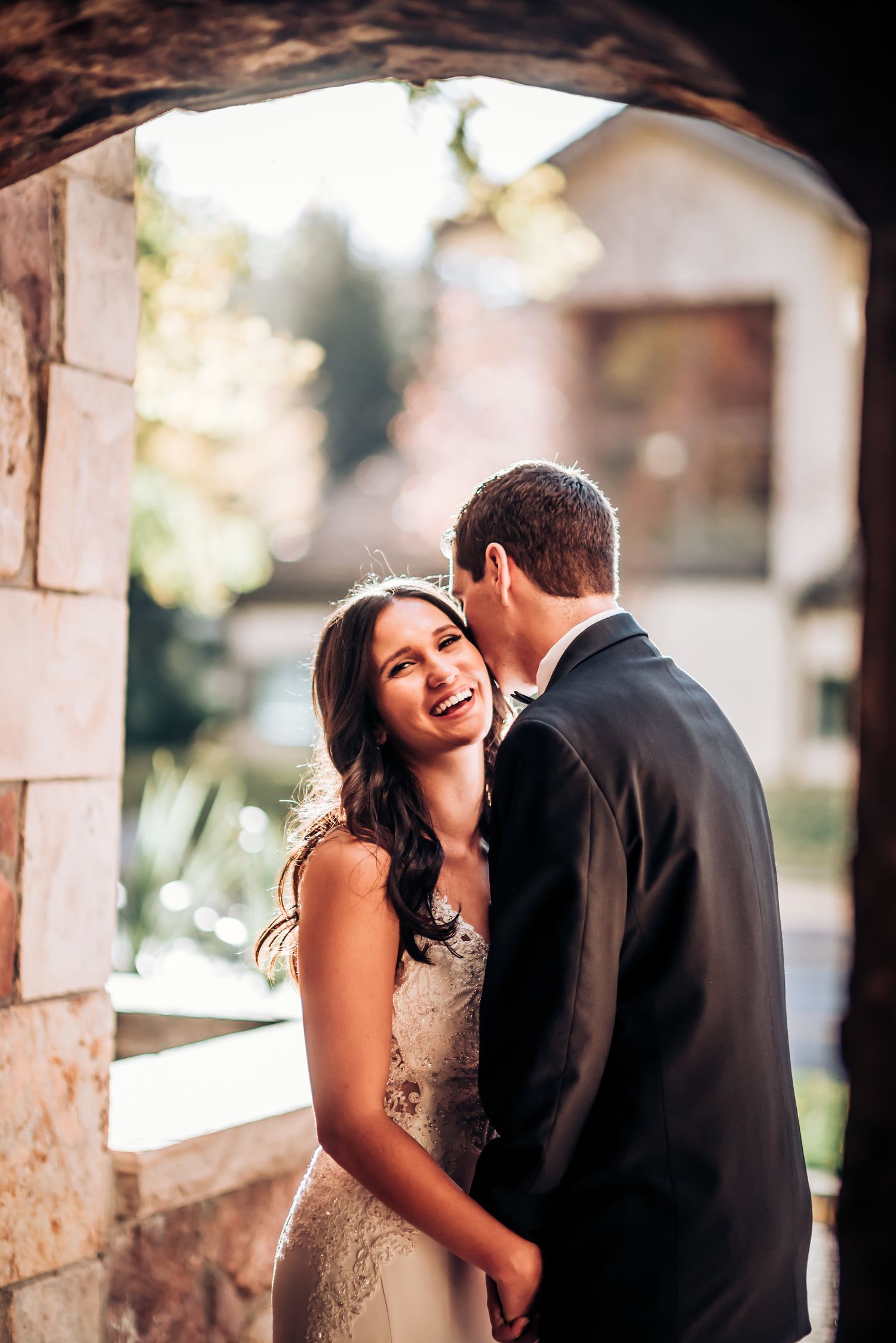 Candid moment between couple under stone archway during wedding photoshoot.