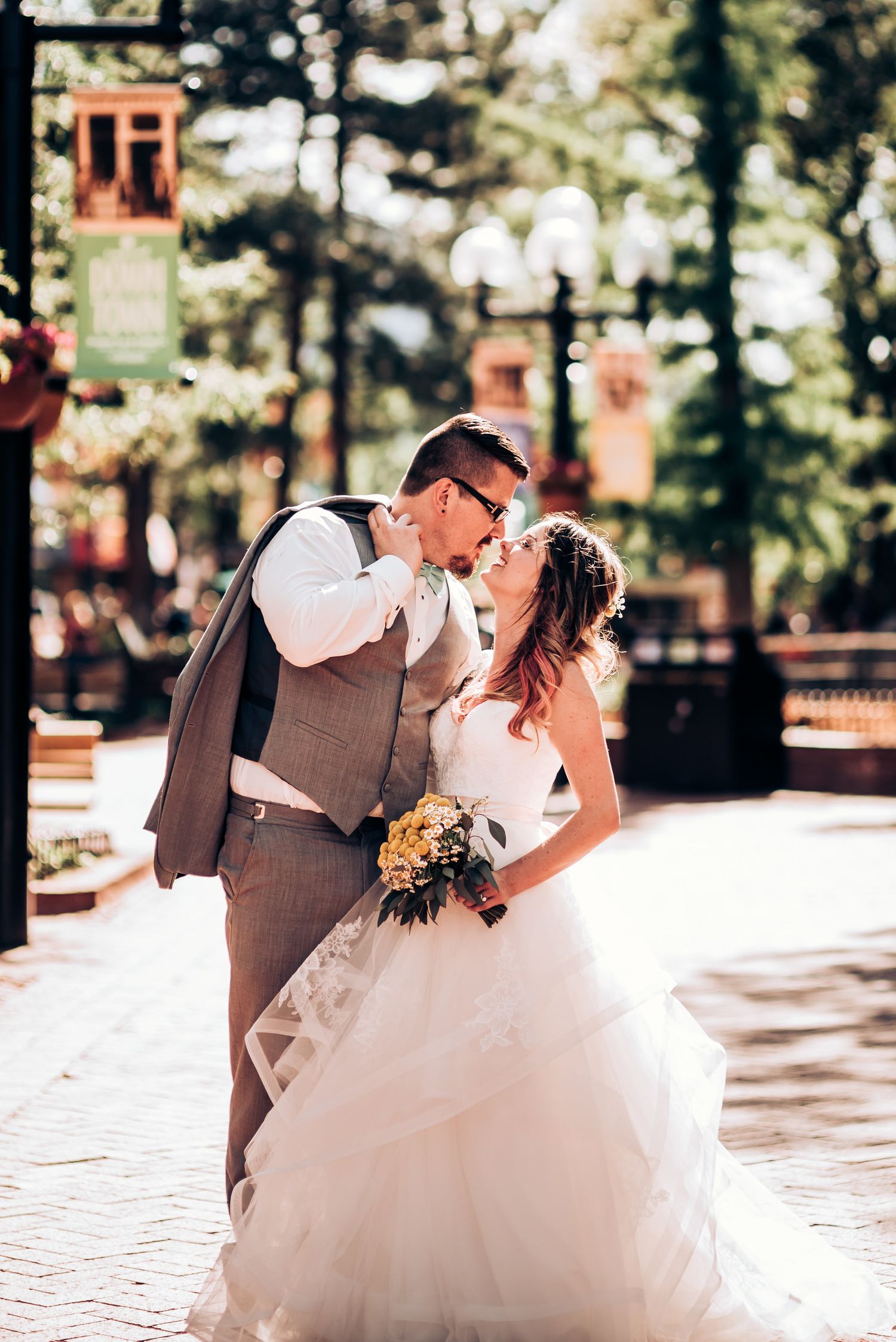 A romantic wedding moment captured outdoors with decorative banners and trees in the background.